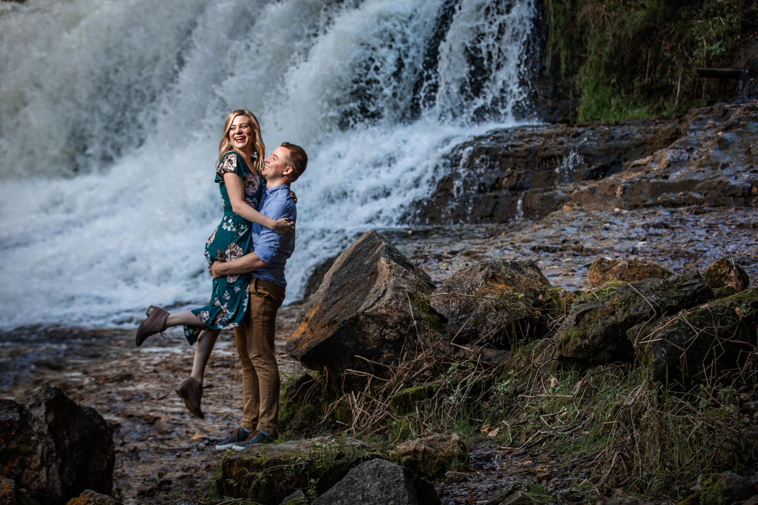 couple playing in front of waterfall for fall engagement