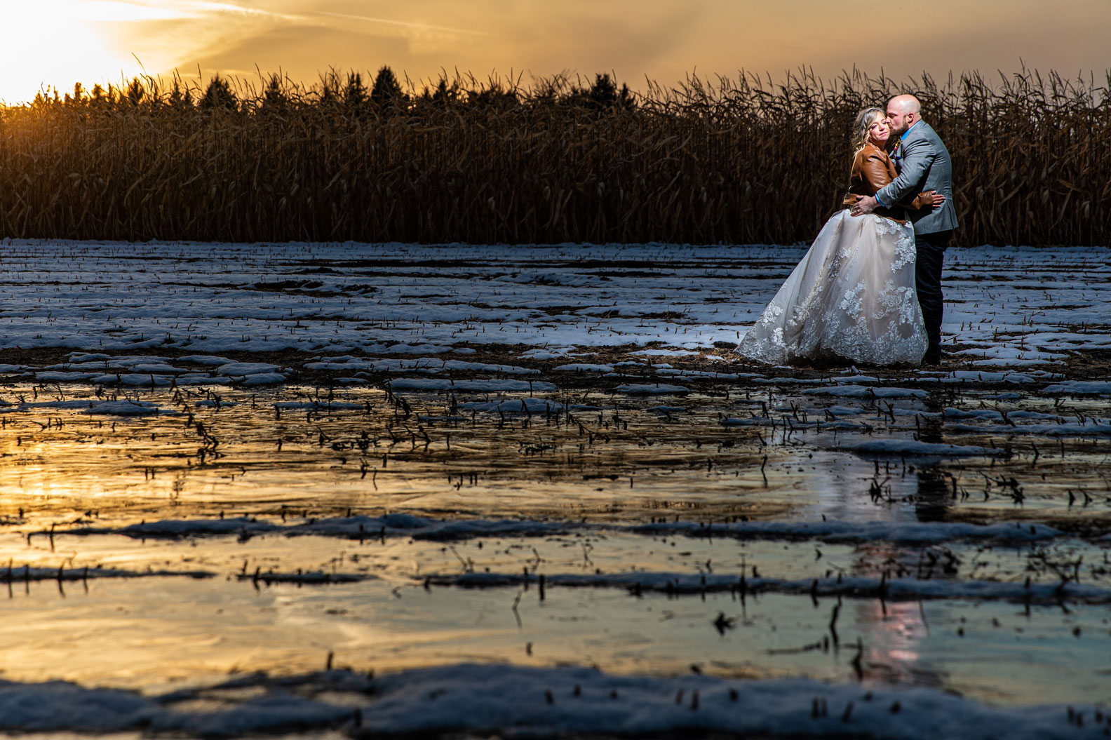wedding couple standing on frozen lake near cornfield at sunset
