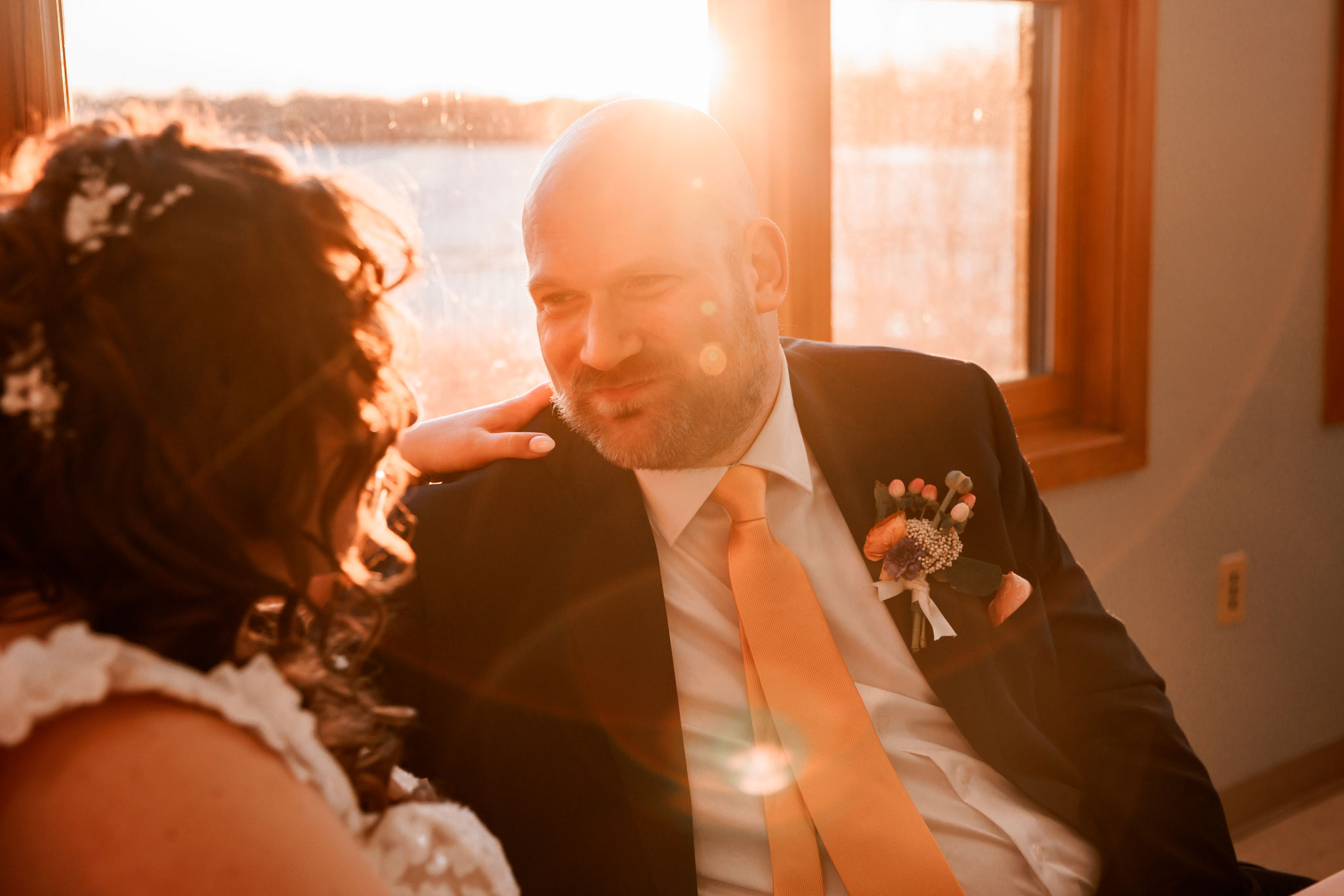 A groom looks lovingly at his new bride at their wedding reception as the sun shines through the window.