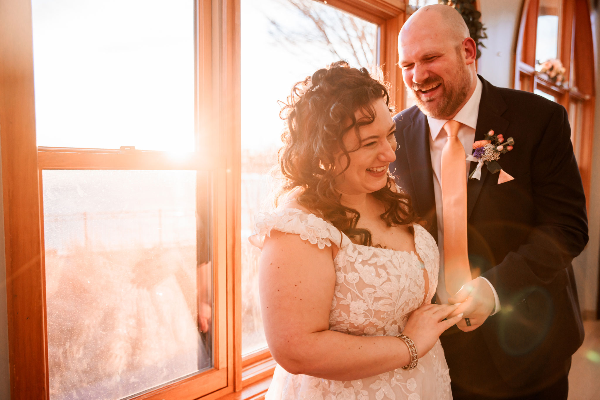 Bride and groom laughing with sunflare in the background.