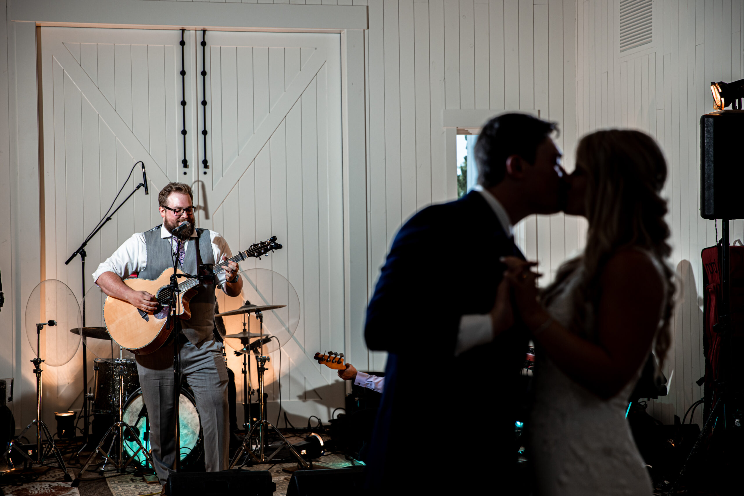 Bride and groom are silhouetted in the foreground while the background focusses on a groomsman playing the guitar on the stage.
