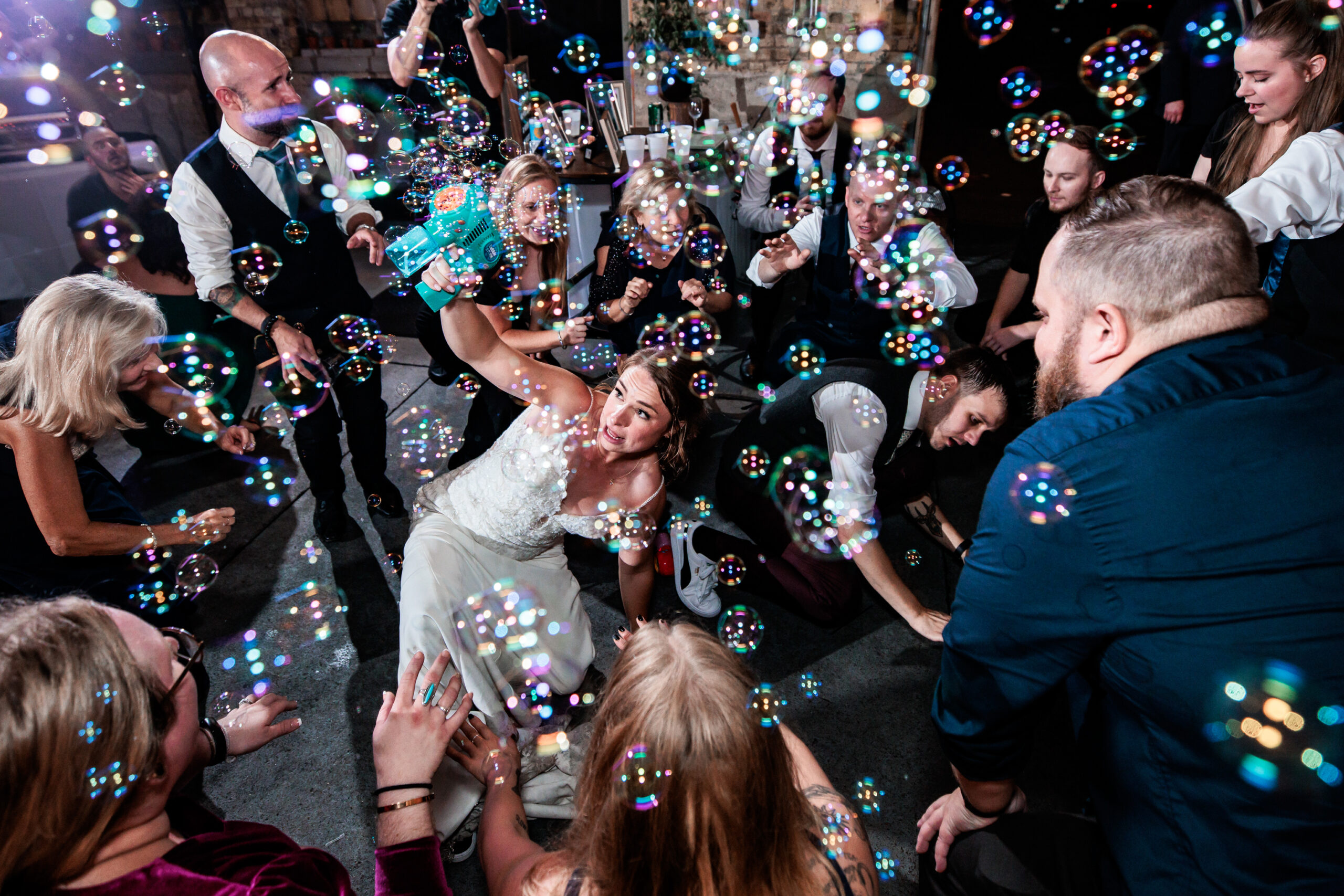 A bride is surrounded by her guests on the dance floor as she fills the room with bubbles.