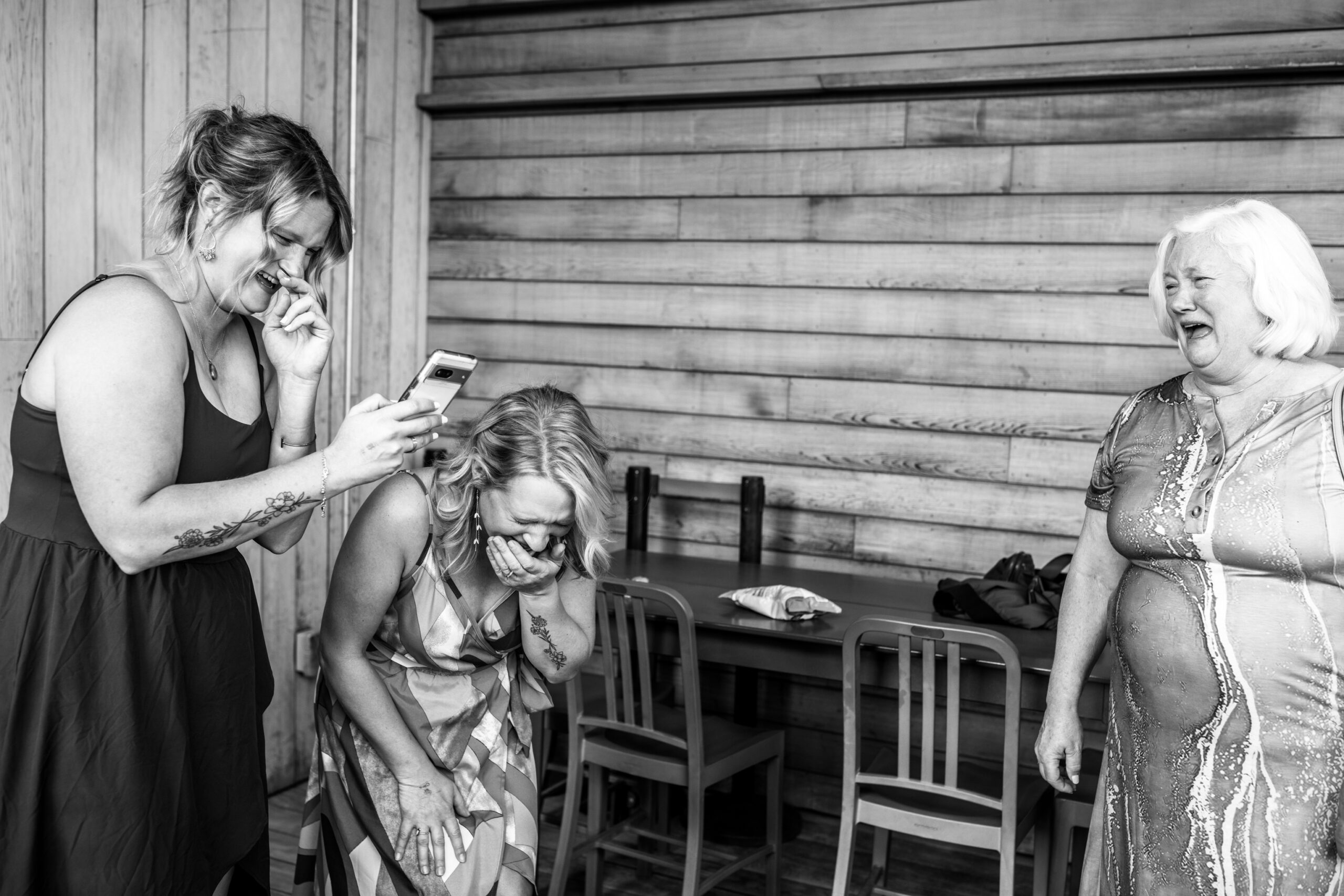 Three women bursting out laughing at an image on a phone during a cocktail hour at Surly brewery.