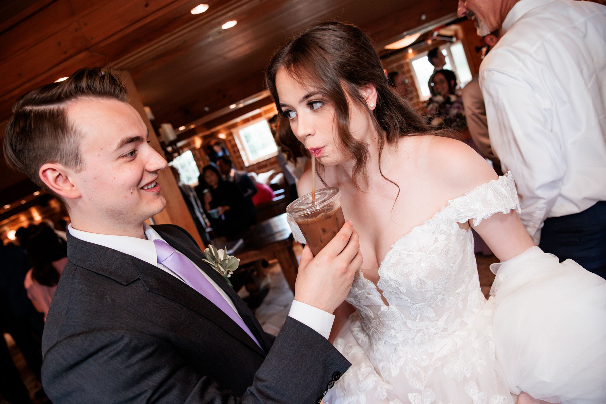 Groom holds iced coffee for bride to sip at the coffee bar.