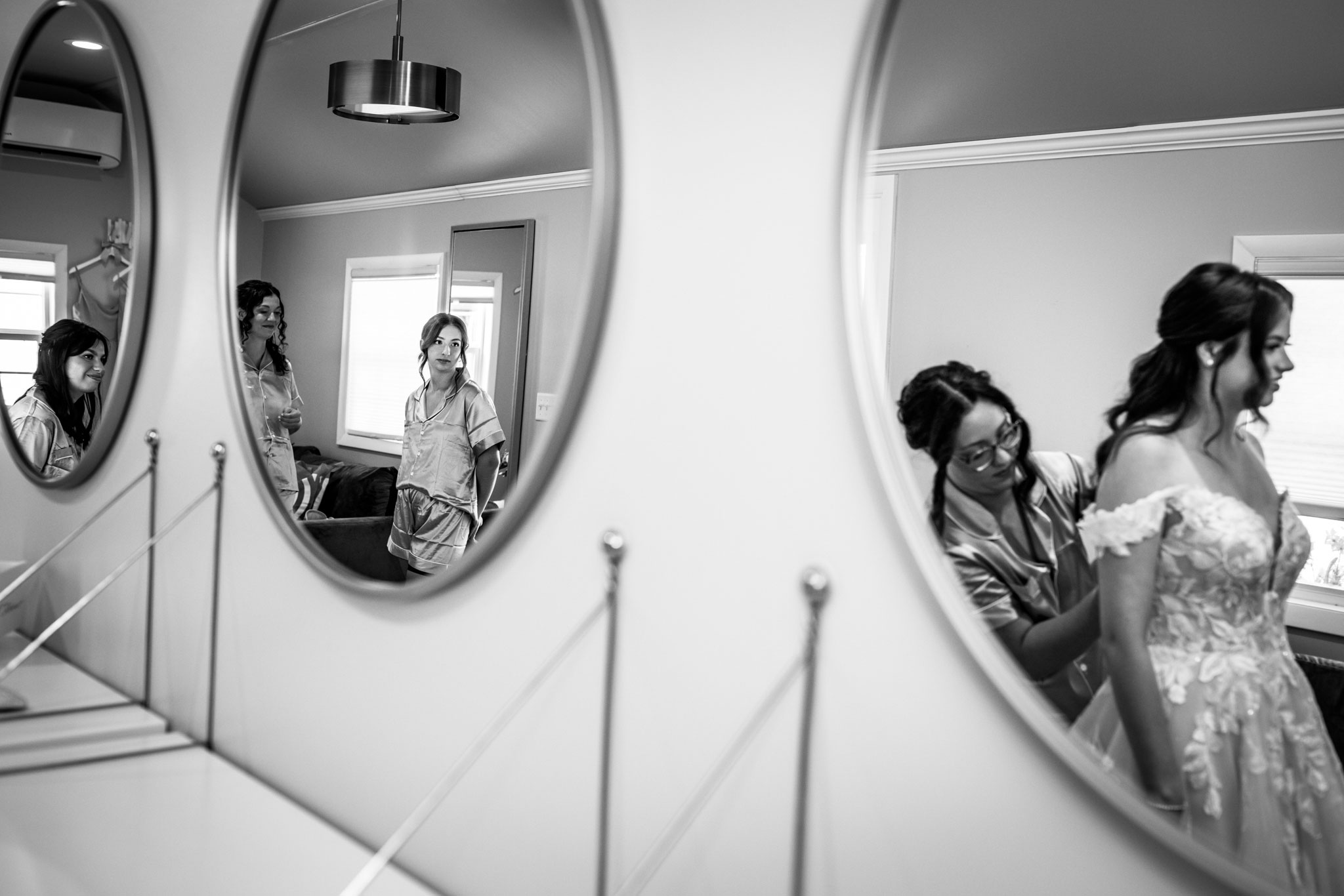 Bride getting ready and her bridesmaids caught in the two mirrors watching.