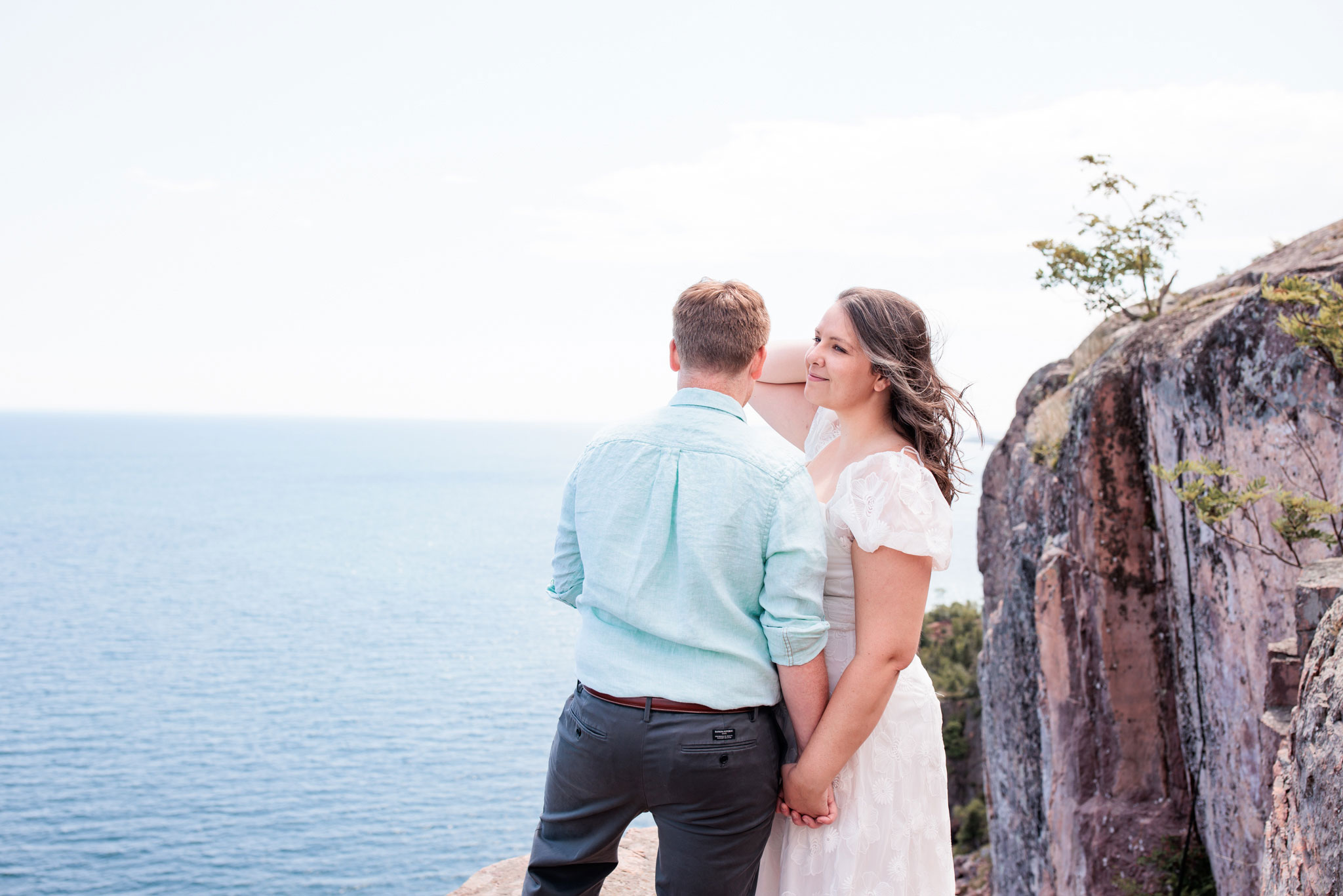A woman looks lovingly at her husband on the cliffside of Palisade head MN.