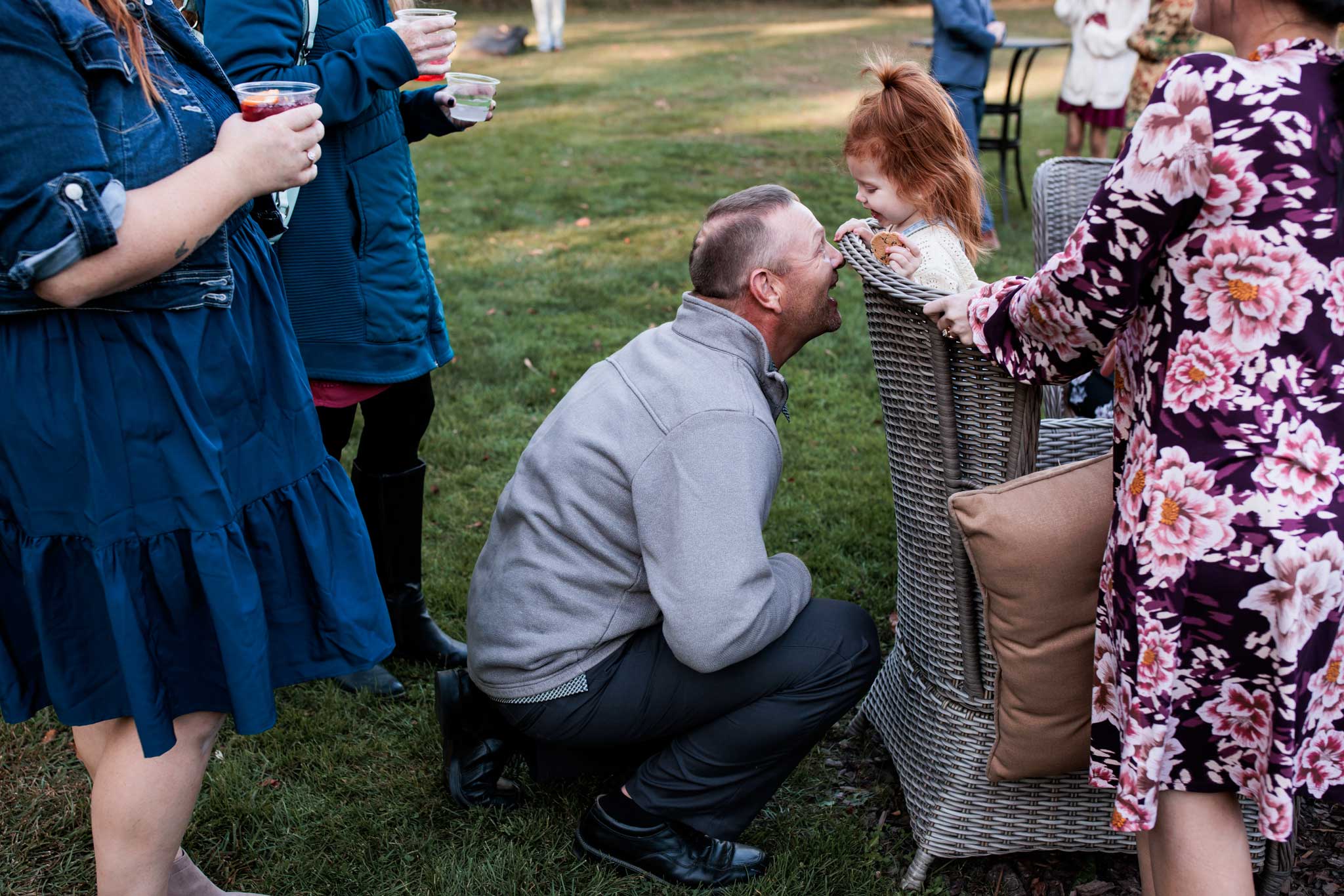 A father plays peek-a-boo with little girl at ourdoor garden wedding reception.