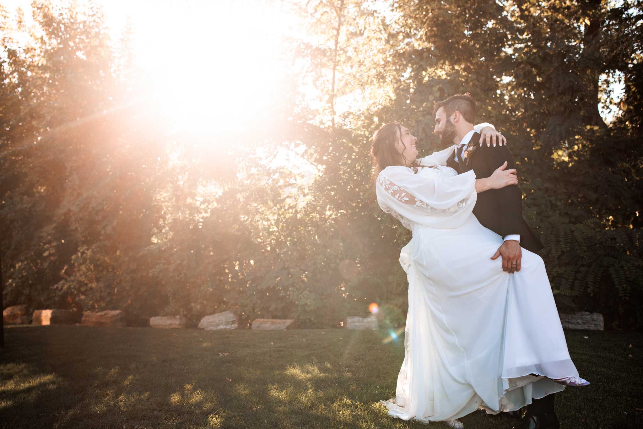 A groom dips his bride outside with the sun flare coming through the trees.