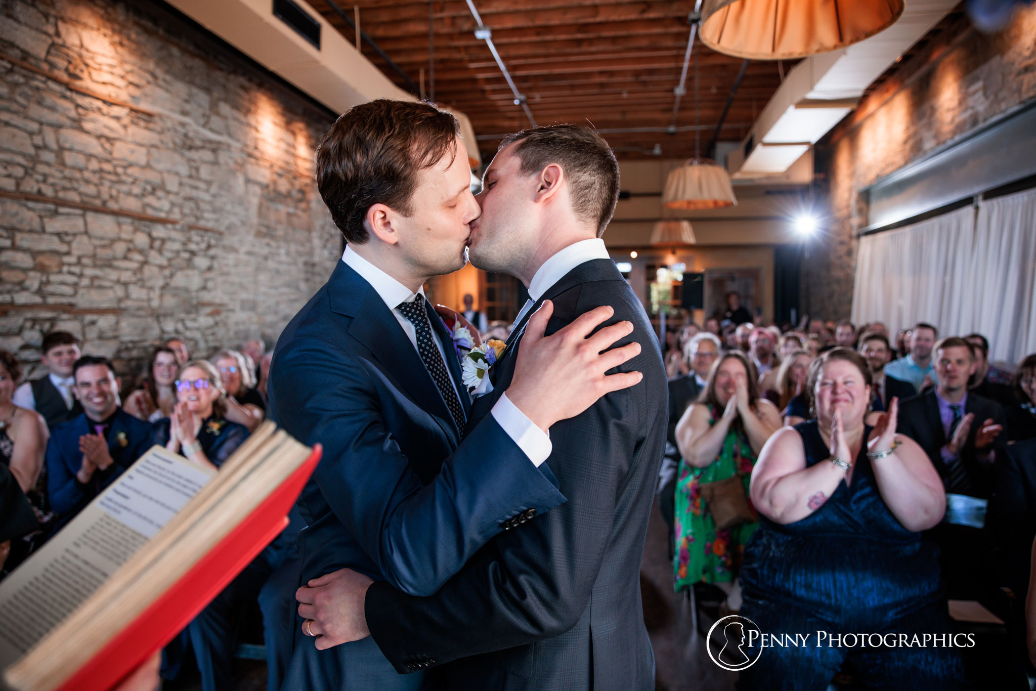 Two grooms first kiss at wedding ceremony inside Aster Cafe.